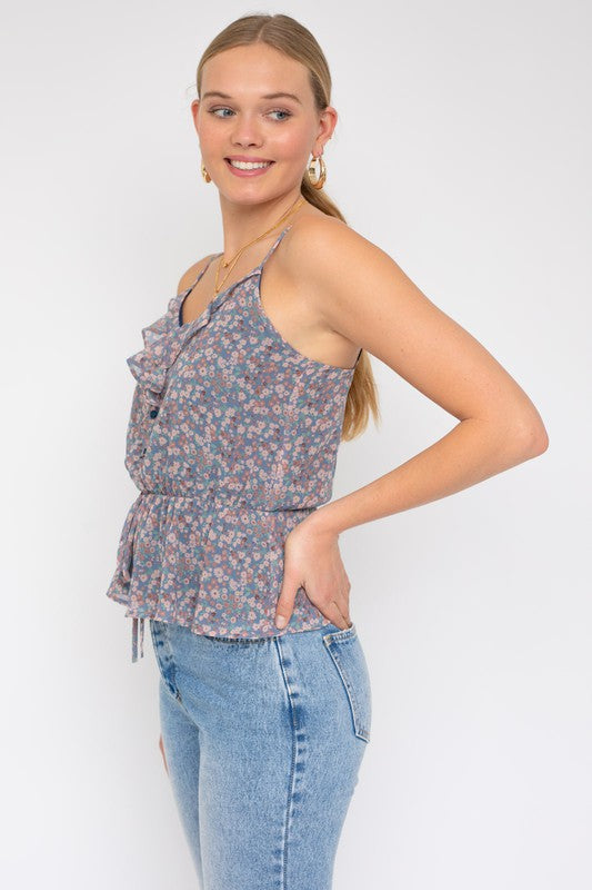 A person wearing a Sleeveless Elastic Waist Top With Ruffle, showcasing a floral pattern, paired with light blue jeans, stands against a white background.