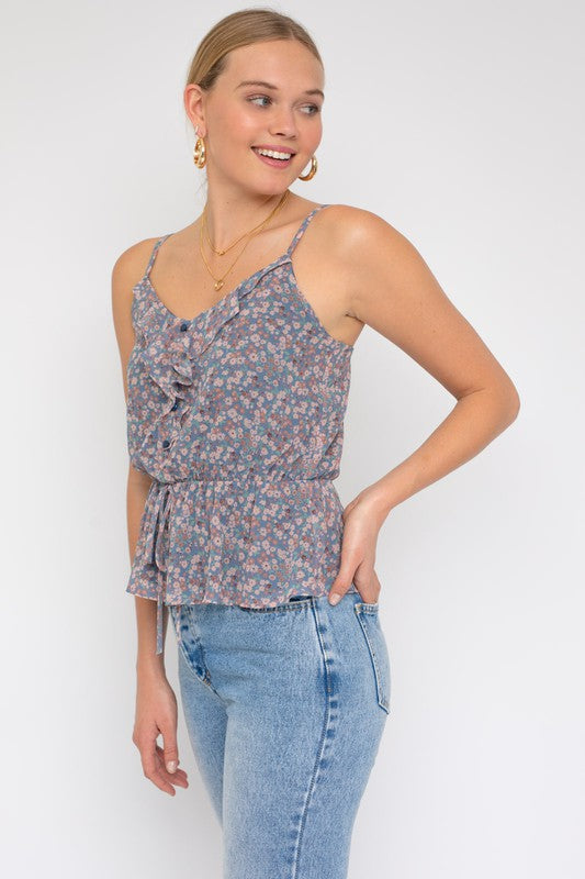 A person wearing a Sleeveless Elastic Waist Top With Ruffle, showcasing a floral pattern, paired with light blue jeans, stands against a white background.