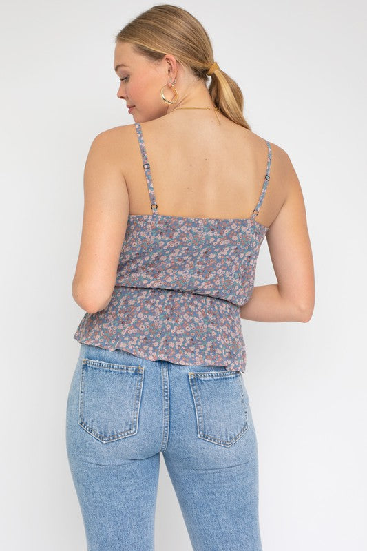 A person wearing a Sleeveless Elastic Waist Top With Ruffle, showcasing a floral pattern, paired with light blue jeans, stands against a white background.