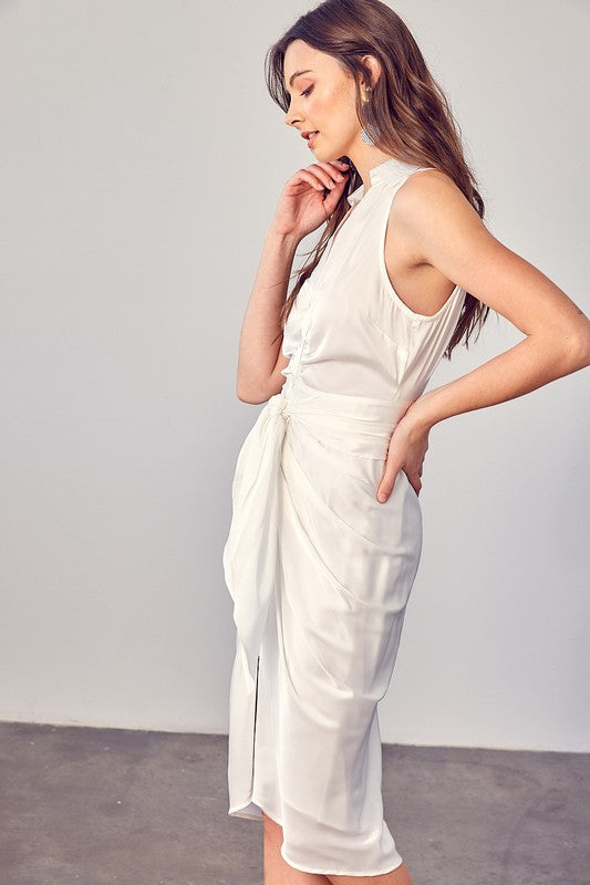 A woman stands indoors against a plain background, elegantly wearing the Sleeveless Collared Front Tie Dress in white.