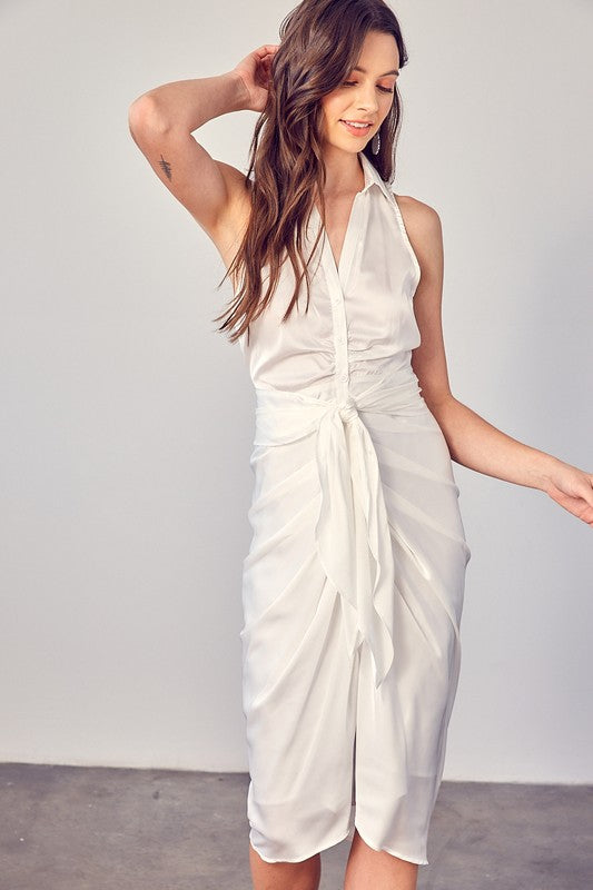 A woman stands indoors against a plain background, elegantly wearing the Sleeveless Collared Front Tie Dress in white.