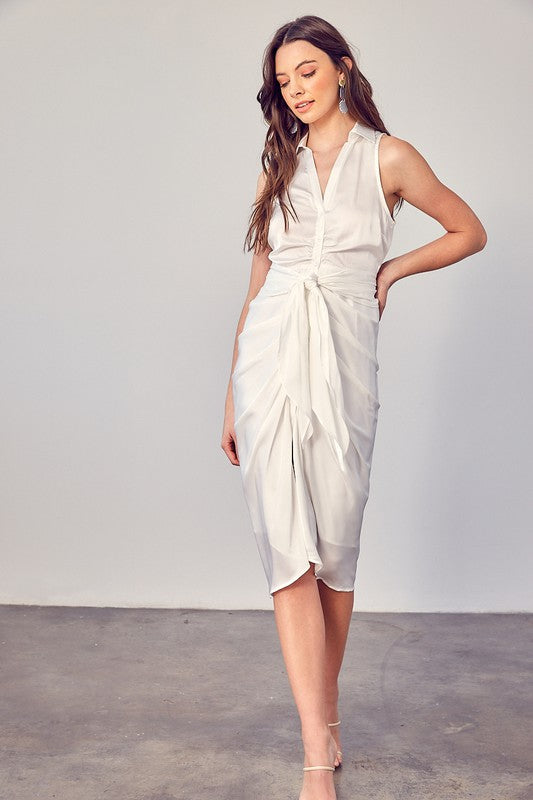 A woman stands indoors against a plain background, elegantly wearing the Sleeveless Collared Front Tie Dress in white.