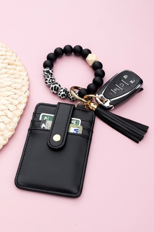A person wearing a Silicone Key Ring Wallet Bracelet holds a small black wallet on a key ring, showcasing a hands-free design.