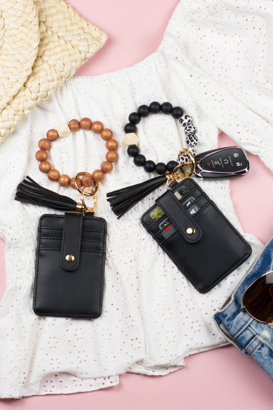 A person wearing a Silicone Key Ring Wallet Bracelet holds a small black wallet on a key ring, showcasing a hands-free design.