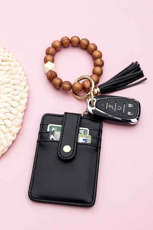 A person wearing a Silicone Key Ring Wallet Bracelet holds a small black wallet on a key ring, showcasing a hands-free design.