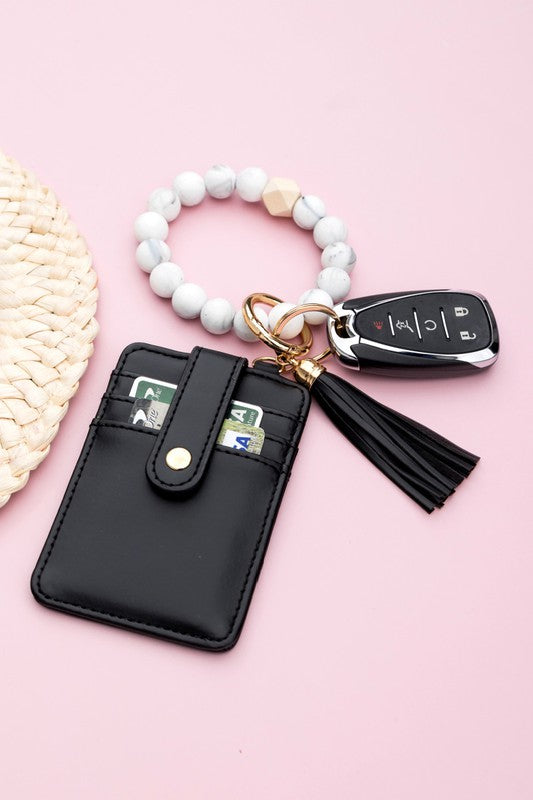 A person wearing a Silicone Key Ring Wallet Bracelet holds a small black wallet on a key ring, showcasing a hands-free design.