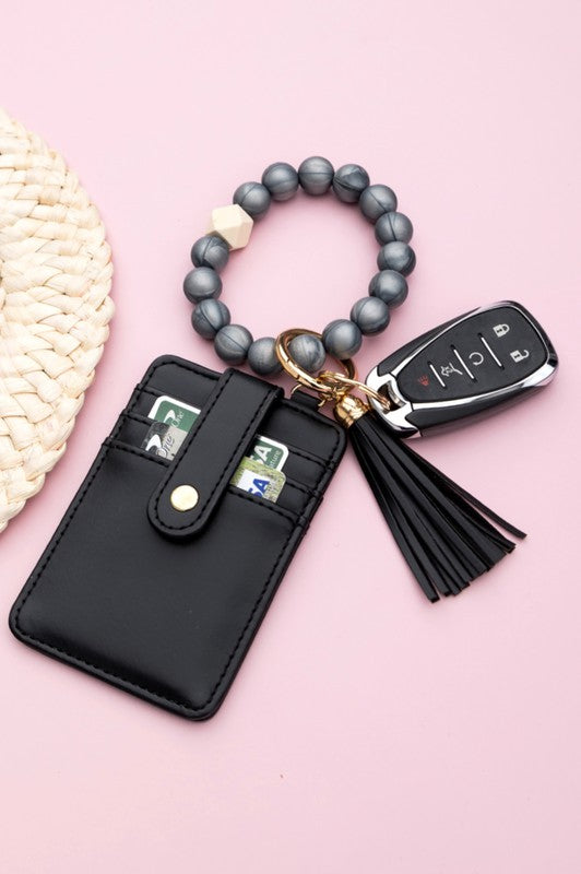 A person wearing a Silicone Key Ring Wallet Bracelet holds a small black wallet on a key ring, showcasing a hands-free design.
