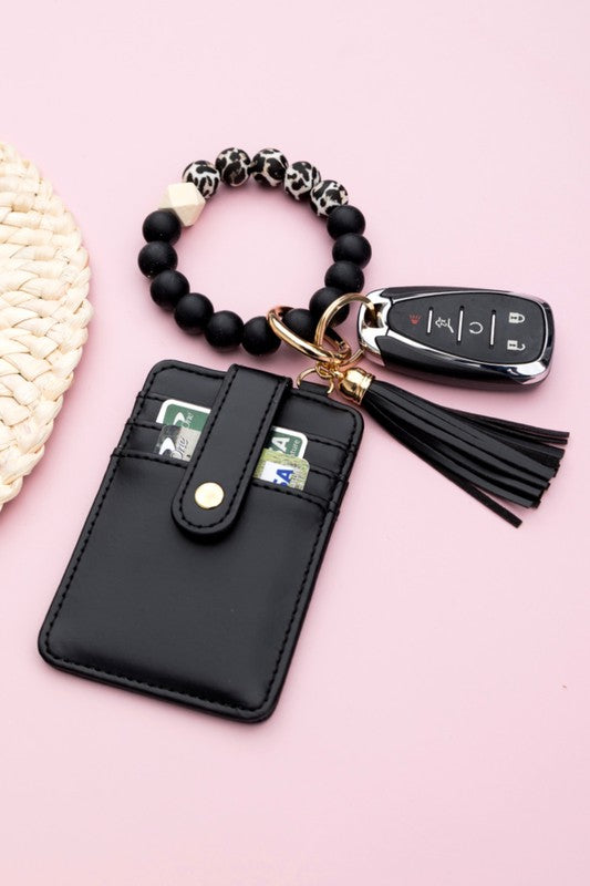A person wearing a Silicone Key Ring Wallet Bracelet holds a small black wallet on a key ring, showcasing a hands-free design.