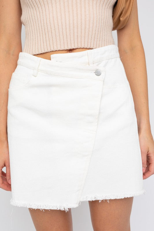 Person wearing a chic summer wardrobe featuring a white denim mini skirt and a light top, standing against a plain background.