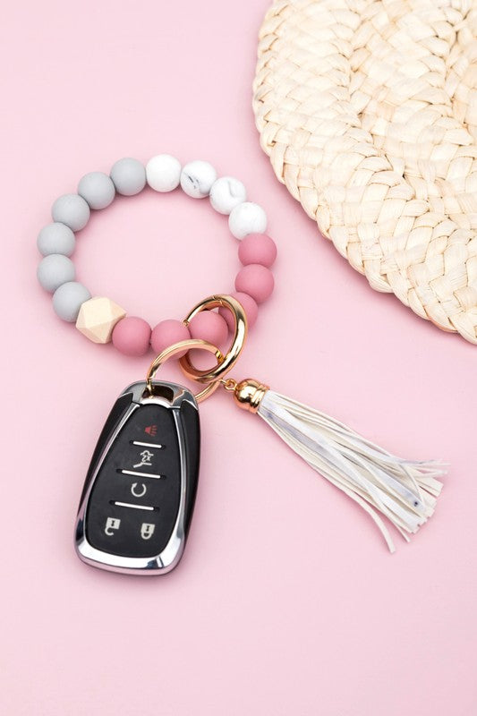 A close-up of a person's wrist adorned with a Silicone Color Block Key Ring Bracelet, featuring a color block design and beads, resting on their denim-clad knee.
