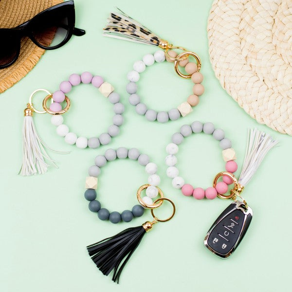 A close-up of a person's wrist adorned with a Silicone Color Block Key Ring Bracelet, featuring a color block design and beads, resting on their denim-clad knee.