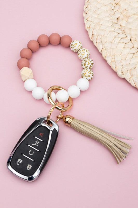 A person wearing a Silicone Gold Leo Key Ring Bracelet holds a car key with a tassel keychain.