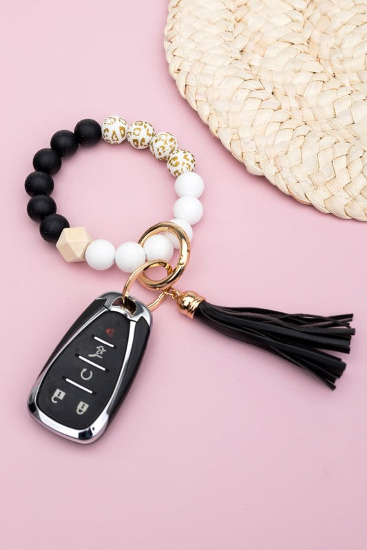 A person wearing a Silicone Gold Leo Key Ring Bracelet holds a car key with a tassel keychain.