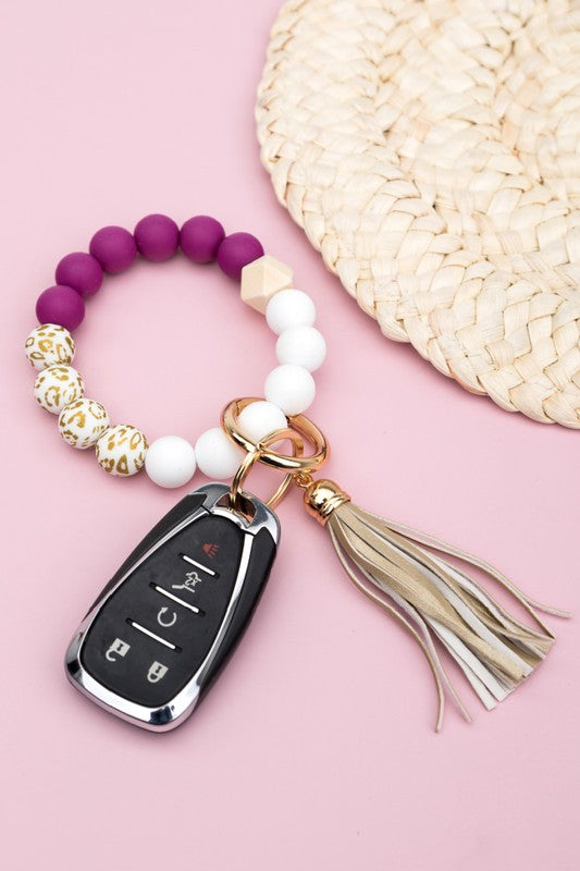 A person wearing a Silicone Gold Leo Key Ring Bracelet holds a car key with a tassel keychain.