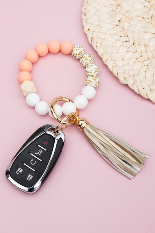 A person wearing a Silicone Gold Leo Key Ring Bracelet holds a car key with a tassel keychain.