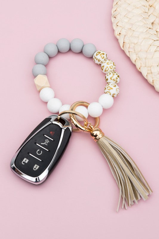 A person wearing a Silicone Gold Leo Key Ring Bracelet holds a car key with a tassel keychain.