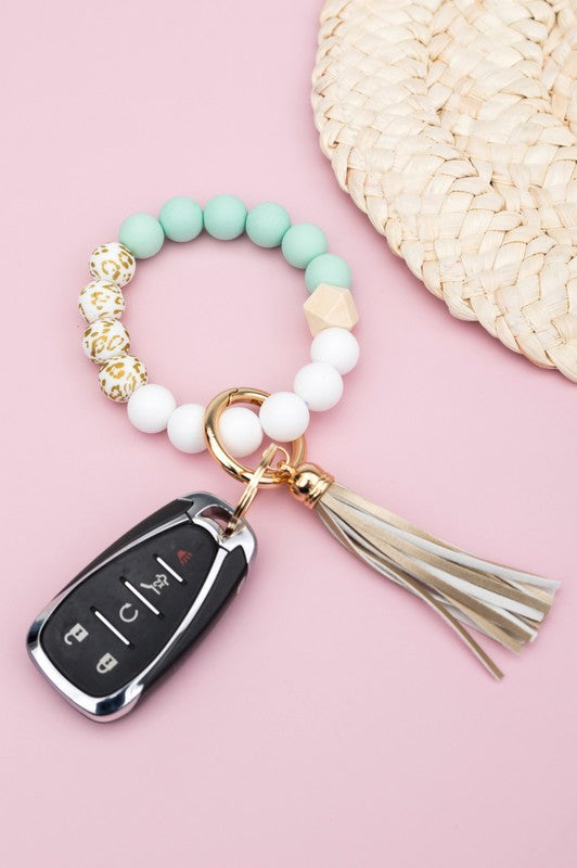 A person wearing a Silicone Gold Leo Key Ring Bracelet holds a car key with a tassel keychain.