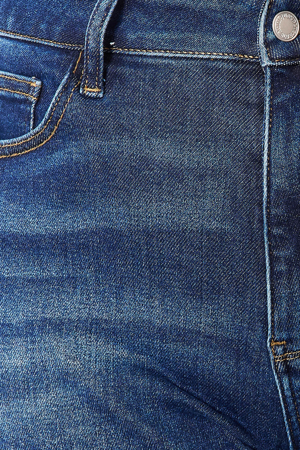 A person wearing Judy Blue Full Size High Waist Released Hem Slit Jeans in indigo wash and a white cropped top stands by a white dresser, showcasing a flattering fit.