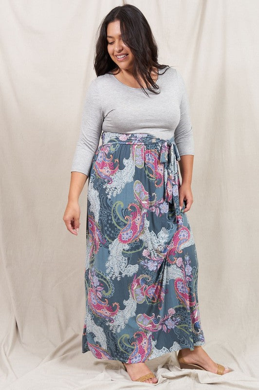 A woman with long hair is wearing the Sash Maxi Dress With Pockets, featuring white and black horizontal stripes and a patterned design. She is standing against a plain background, looking to the side.