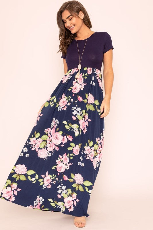 Against a plain backdrop, a woman is dressed in a Short Sleeve Floral Maxi Dress, which stylishly merges short sleeves with its elegant, flowing design.