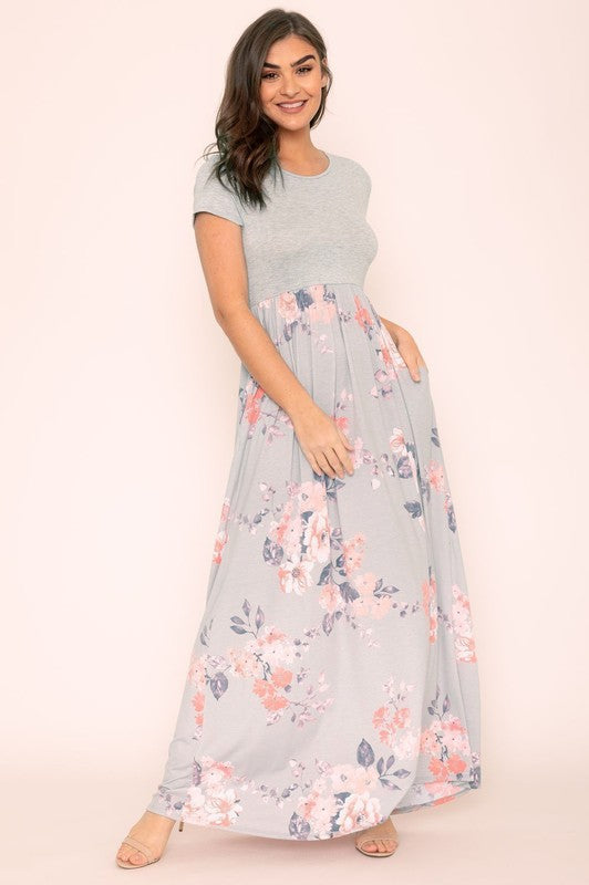 Against a plain backdrop, a woman is dressed in a Short Sleeve Floral Maxi Dress, which stylishly merges short sleeves with its elegant, flowing design.