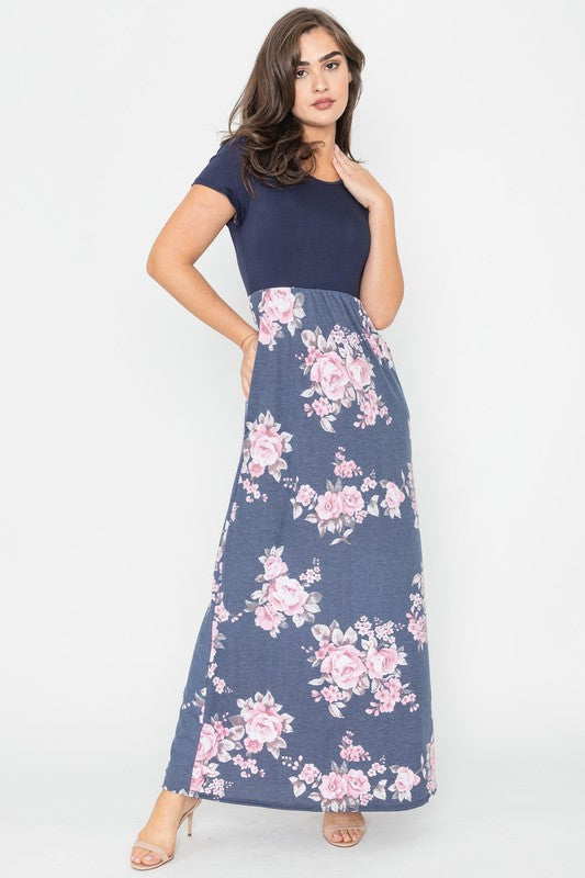 A woman wearing the Plus Short Sleeve Floral Maxi Dress stands smiling, her hands slightly above her waist, against a plain background. Made in the United States, her attire exudes charm and elegance.