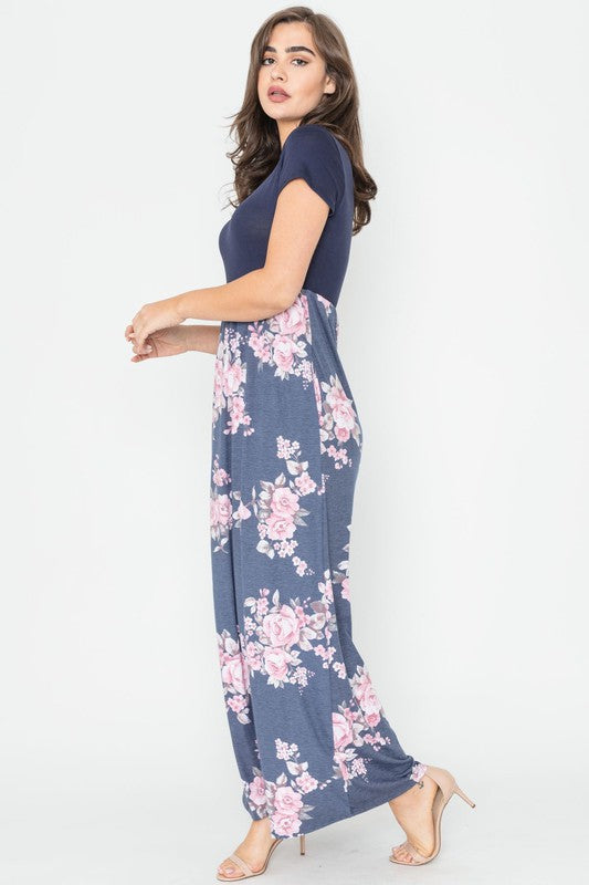 A woman wearing the Plus Short Sleeve Floral Maxi Dress stands smiling, her hands slightly above her waist, against a plain background. Made in the United States, her attire exudes charm and elegance.