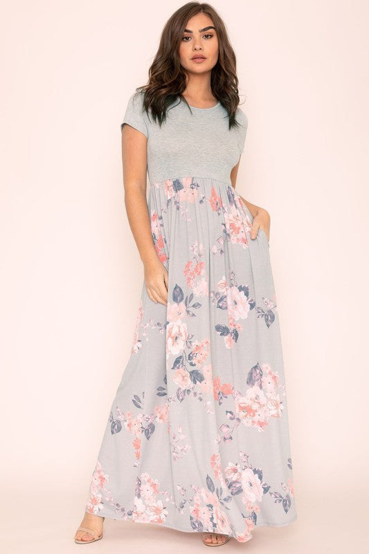 A woman wearing the Plus Short Sleeve Floral Maxi Dress stands smiling, her hands slightly above her waist, against a plain background. Made in the United States, her attire exudes charm and elegance.