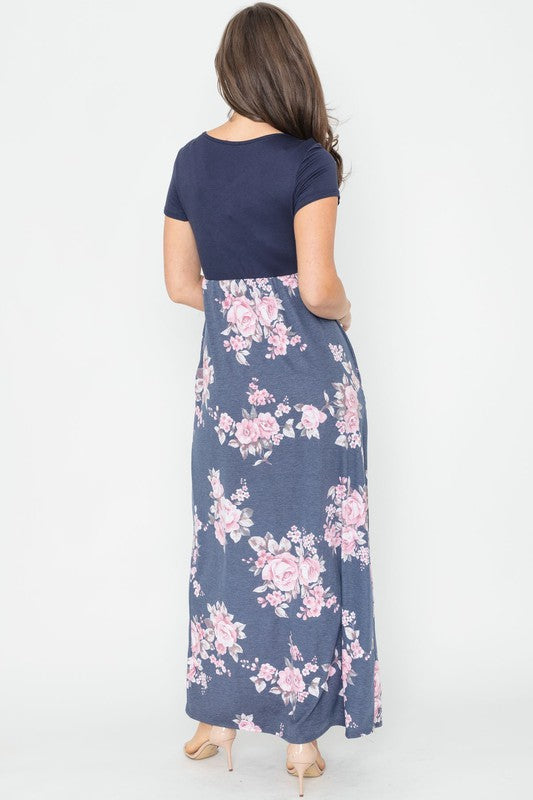 A woman wearing the Plus Short Sleeve Floral Maxi Dress stands smiling, her hands slightly above her waist, against a plain background. Made in the United States, her attire exudes charm and elegance.