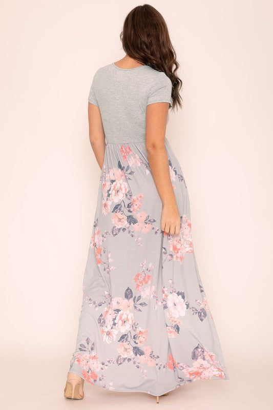 A woman wearing the Plus Short Sleeve Floral Maxi Dress stands smiling, her hands slightly above her waist, against a plain background. Made in the United States, her attire exudes charm and elegance.