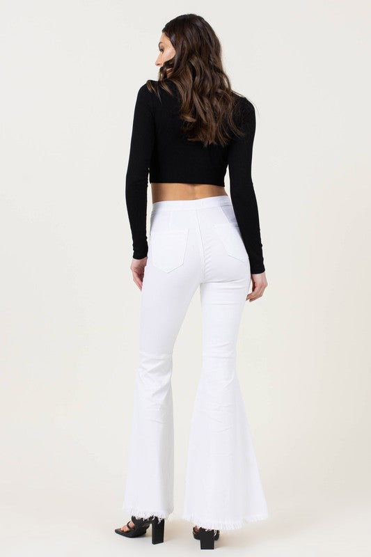 A woman stands against a plain background wearing high-waisted flare jeans and a black long-sleeve top.