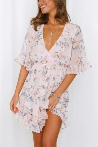 A woman is wearing a Floral Printed Ruffled Mini Dress with a V-neck, featuring ruffled sleeves and hem, as she stands against a plain background.