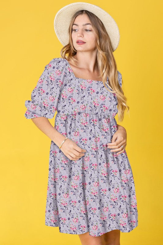 A woman in a Branch Floral Squared Neck Mini Dress and straw hat poses gracefully against a bright yellow background.