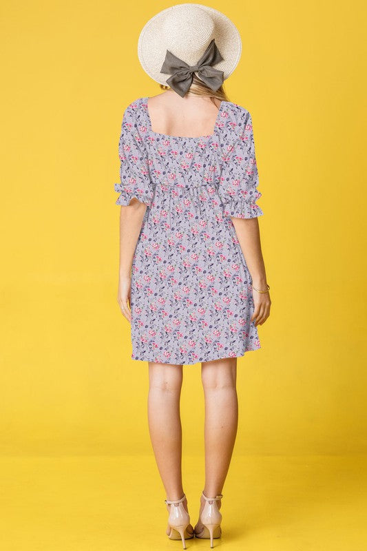 A woman in a Branch Floral Squared Neck Mini Dress and straw hat poses gracefully against a bright yellow background.