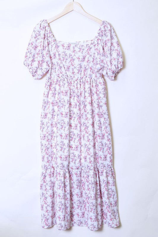 A woman in a Ditsy Floral Square Neck Sundress, crafted from 100% polyester, stands against a yellow background, highlighting its elegant light blue floral design.