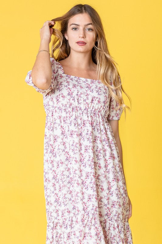 A woman in a Ditsy Floral Square Neck Sundress, crafted from 100% polyester, stands against a yellow background, highlighting its elegant light blue floral design.