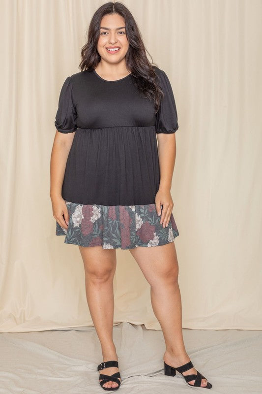 A person wearing the Floral Two Tone Tiered Mini Dress, featuring puff sleeves and a vibrant tie-dye hem, stands against a beige background, smiling.