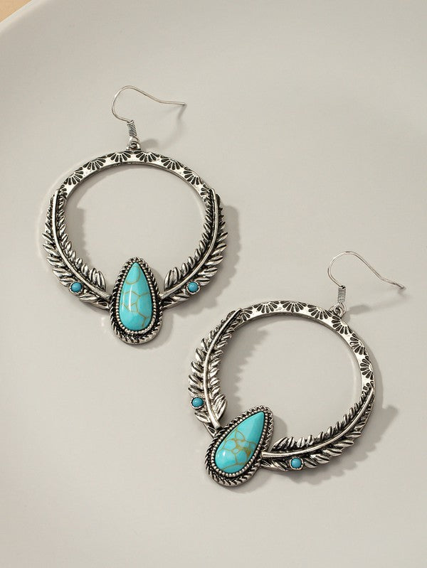 A pair of Boho distressed feather circle earrings in silver, adorned with turquoise teardrop-shaped stones and featuring intricate feather-like detailing, are displayed on a light surface.