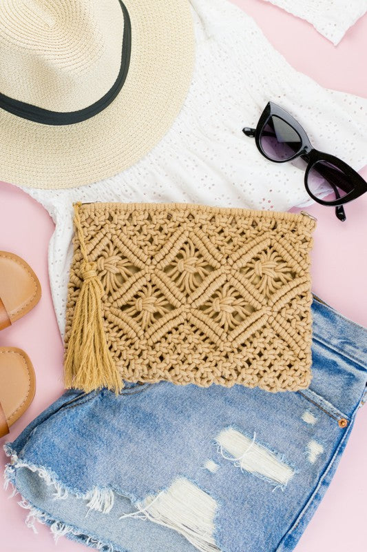 A person sits with the Macrame Tassel Clutch, which showcases a geometric pattern and tassel, secured with a zipper closure. They wear a white top and denim shorts that perfectly complement this stylish accessory.