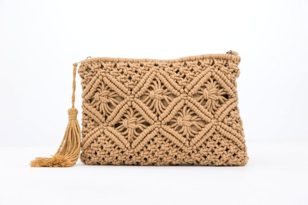 A person sits with the Macrame Tassel Clutch, which showcases a geometric pattern and tassel, secured with a zipper closure. They wear a white top and denim shorts that perfectly complement this stylish accessory.