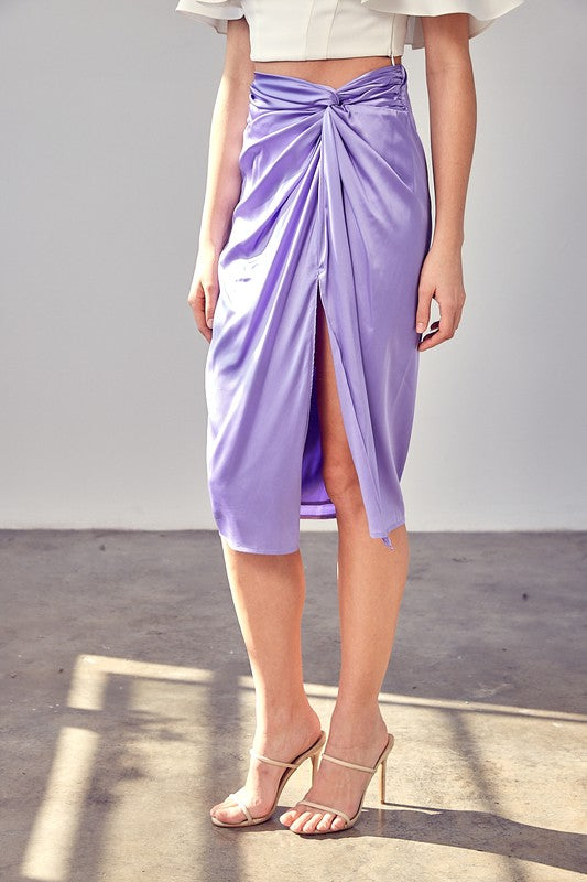 A person wearing the Side Gathered Slit Skirt in lavender paired with a white top, standing on a sunlit floor.