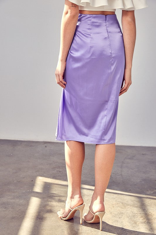 A person wearing the Side Gathered Slit Skirt in lavender paired with a white top, standing on a sunlit floor.