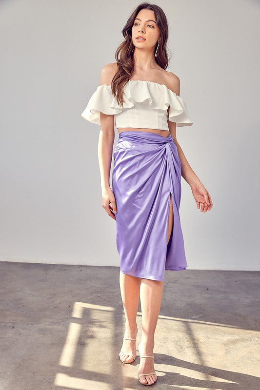 A person wearing the Side Gathered Slit Skirt in lavender paired with a white top, standing on a sunlit floor.