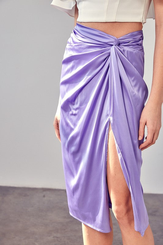 A person wearing the Side Gathered Slit Skirt in lavender paired with a white top, standing on a sunlit floor.