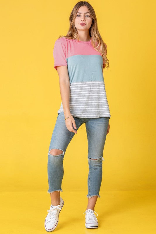 A person in a Sage Coral Black Grey Stripe Lavender Top made of polyester and jeans stands in a room with plants and white curtains.