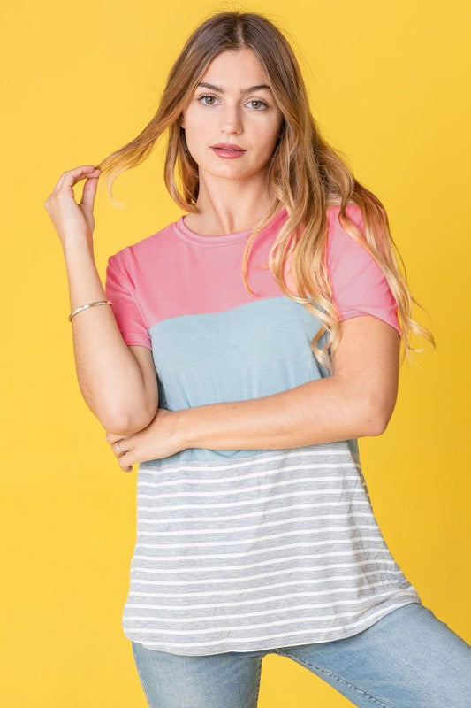 A person in a Sage Coral Black Grey Stripe Lavender Top made of polyester and jeans stands in a room with plants and white curtains.