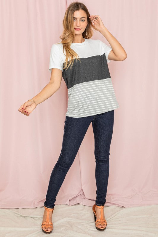 A person in a Sage Coral Black Grey Stripe Lavender Top made of polyester and jeans stands in a room with plants and white curtains.