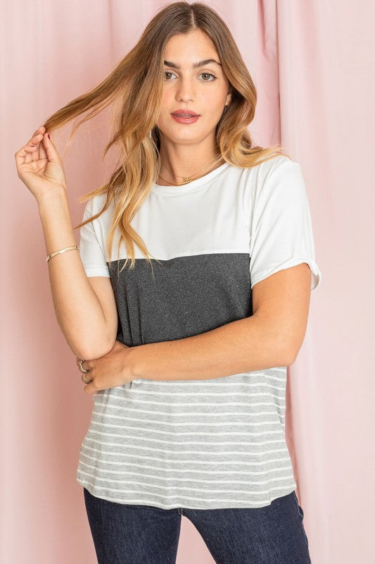 A person in a Sage Coral Black Grey Stripe Lavender Top made of polyester and jeans stands in a room with plants and white curtains.