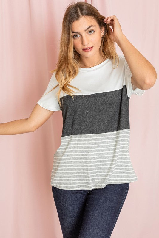 A person in a Sage Coral Black Grey Stripe Lavender Top made of polyester and jeans stands in a room with plants and white curtains.