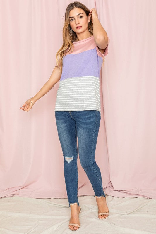 A person in a Sage Coral Black Grey Stripe Lavender Top made of polyester and jeans stands in a room with plants and white curtains.